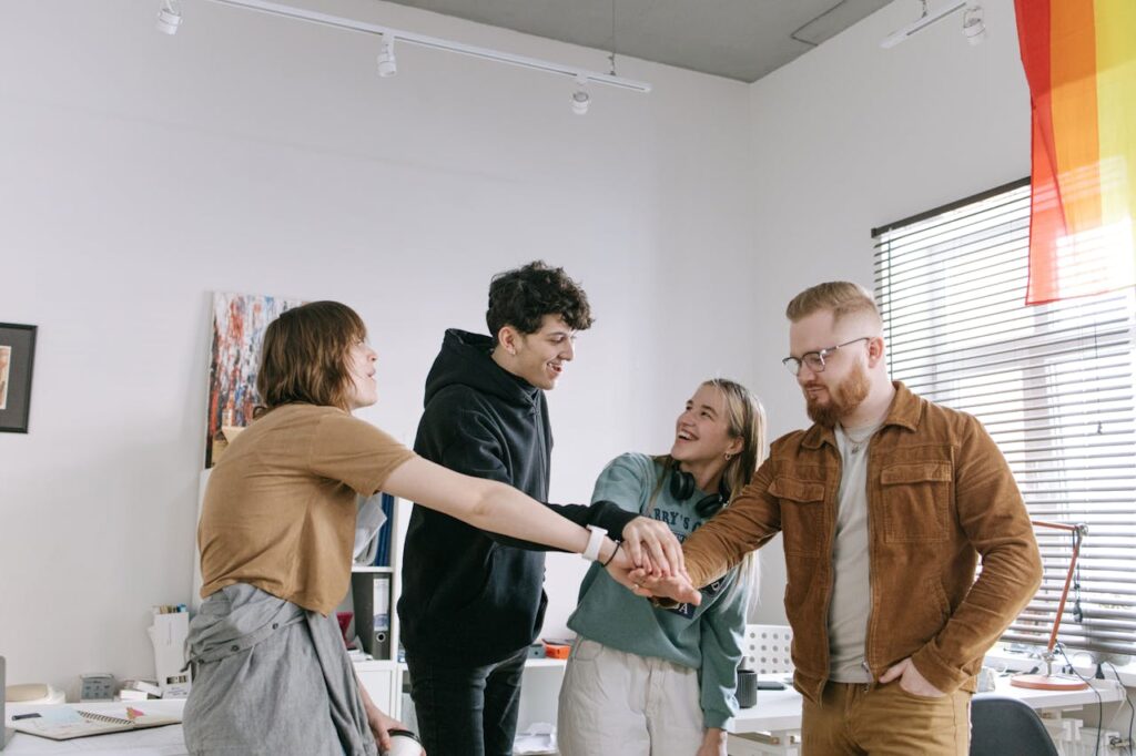 A group of four young people in an office, stacking their hands together in a team-building gesture.