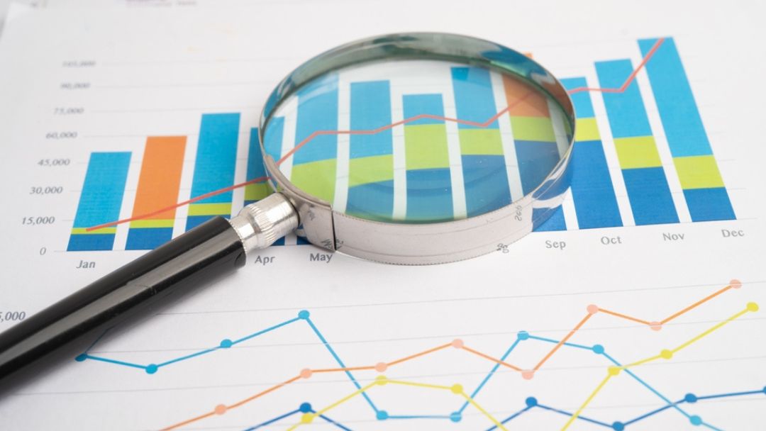 Magnifying glass examining detailed business analytics and financial charts showing importance of market research for informed decisions