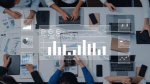 Infographic of business team analyzing data around conference table: holographic charts, graphs, pie charts, bar graphs, and metrics overlay the scene with laptops, notebooks, and calculators. Represents data-driven decision making in corporate strategy.